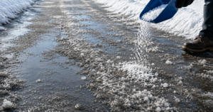 Salt being sprinkled onto a wet, slushy winter walkway after melting ice, illustrating how road salt helps reduce icy surfaces.